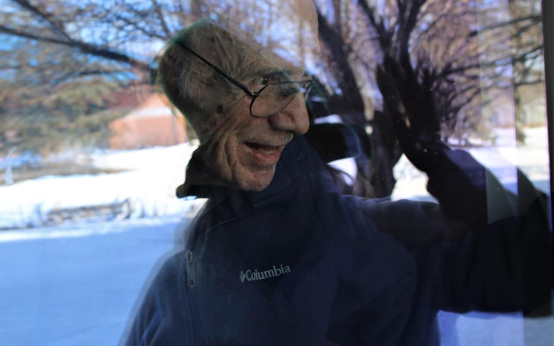 Jim Matchie peers through his window at his daughter Pam Matchie-Thiede in March 2020. Her reflection is visible in the window. C.S. Hagen / The Forum